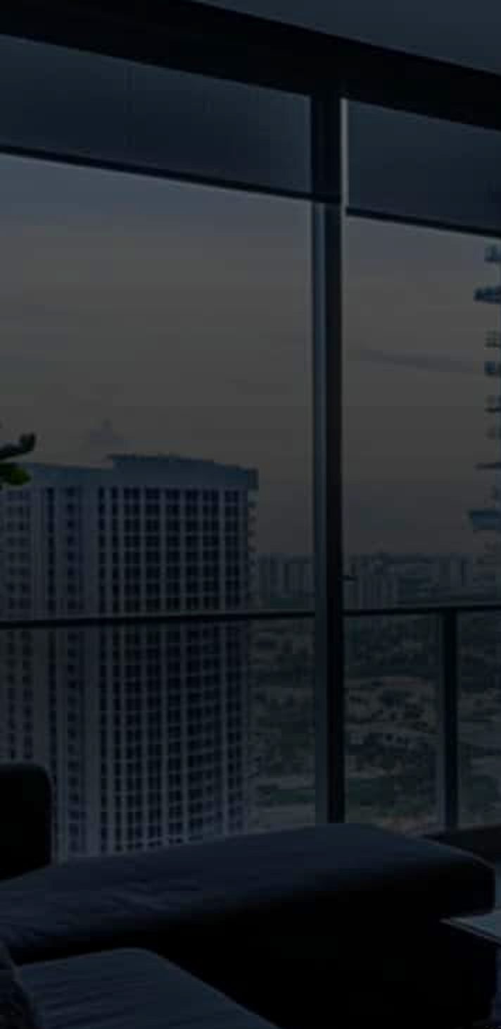 A modern apartment interior at dusk, with floor-to-ceiling windows over the city